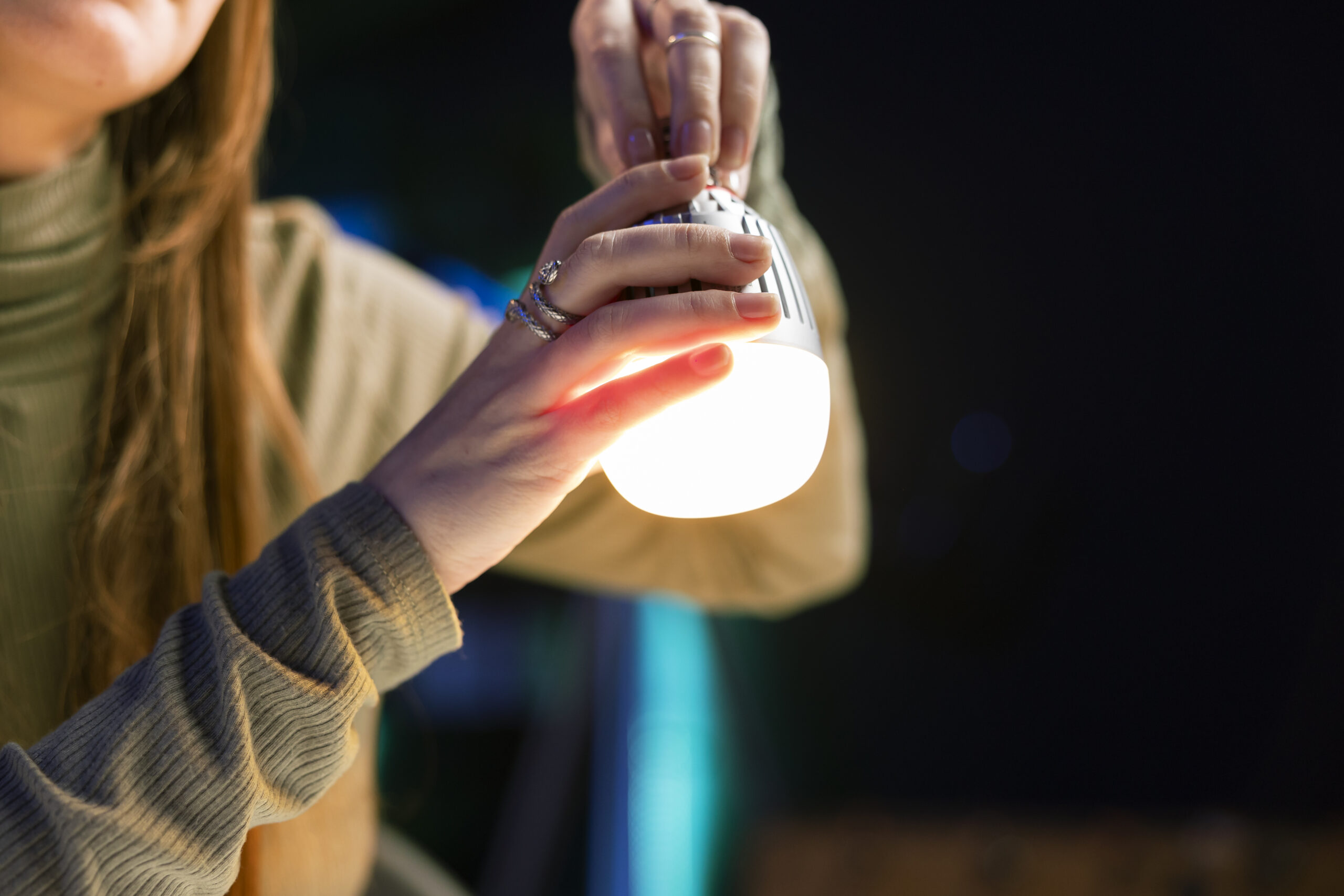 Mujer instalando una bombilla inteligente de luz cálida en un entorno doméstico.