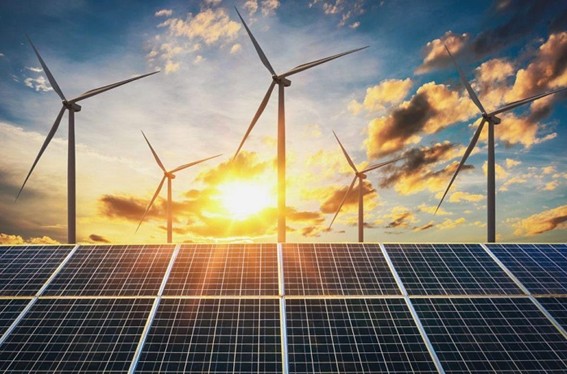 Paneles solares en primer plano y aerogeneradores al fondo con el sol saliendo entre nubes coloridas, simbolizando el uso de energías renovables.