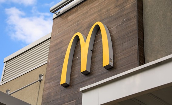Logo amarillo de McDonald’s en la fachada de un local moderno, bajo cielo parcialmente nublado.