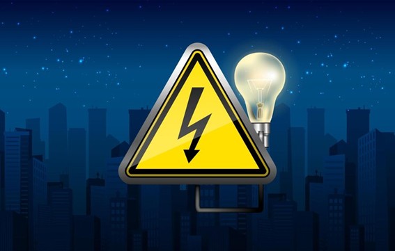 Señal de advertencia de electricidad con un rayo negro sobre fondo amarillo, acompañada de una bombilla encendida y una silueta de ciudad al anochecer.