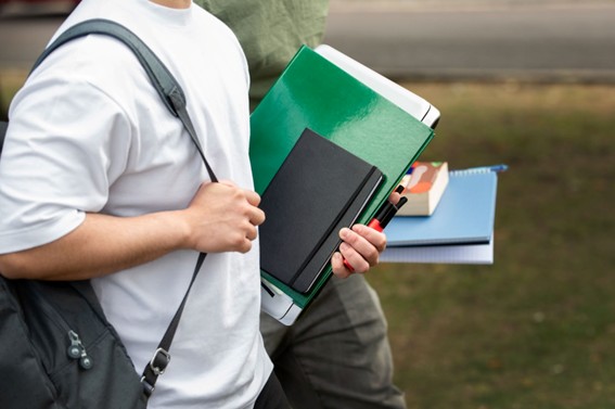 Estudiantes caminando con carpetas, cuadernos y mochilas en un entorno al aire libre.