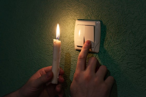 Mano sosteniendo una vela encendida frente a un interruptor de luz durante un corte de energía.