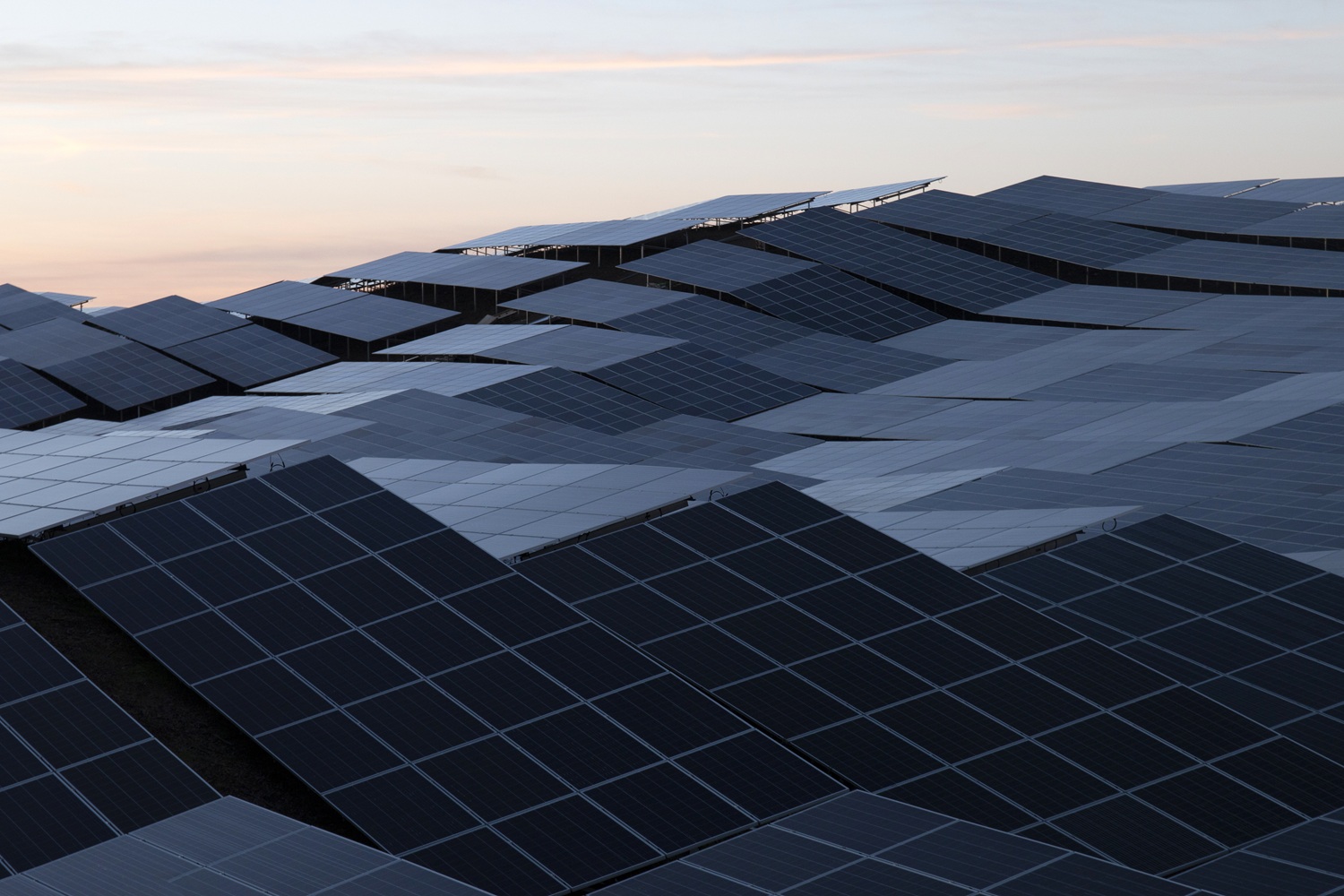 Vista panorámica de un campo de paneles solares dispuestos en varias alturas al atardecer, con cielo claro al fondo.