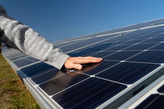 Mano tocando un panel solar en un campo con cielo despejado.