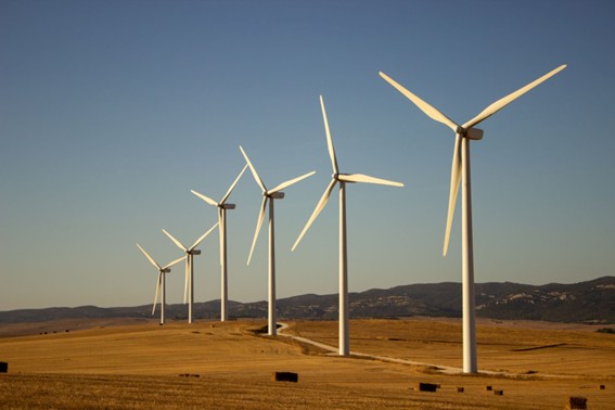 Serie de turbinas eólicas blancas instaladas en un campo seco con montañas al fondo y cielo despejado, representando generación de energía renovable.